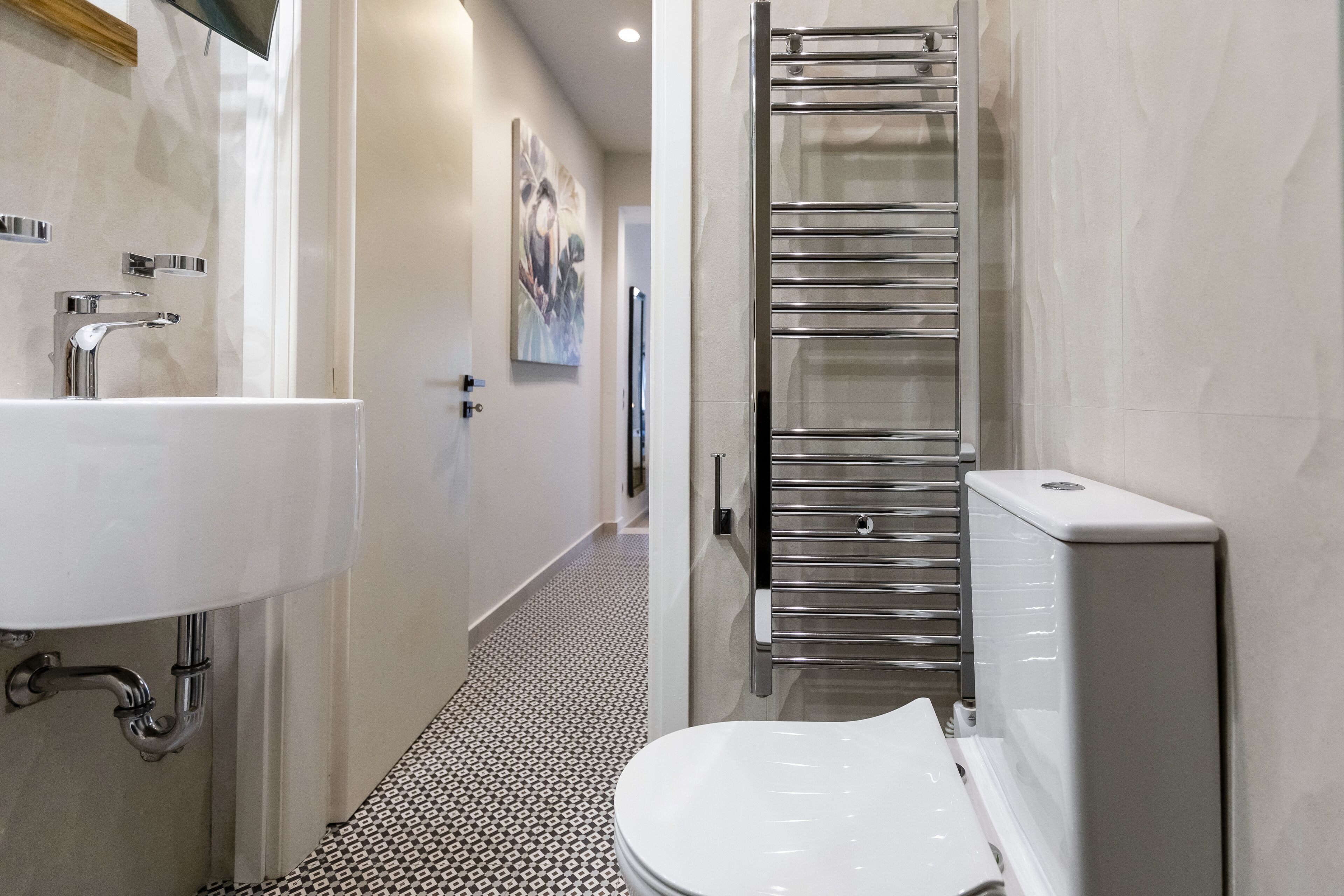 A modern bathroom with a white sink, chrome fixtures, a towel rack, and a patterned floor.