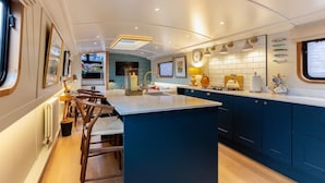 A modern kitchen with a central island, blue cabinets, and a window overlooking the deck. - Luxurious houseboat in London (London)