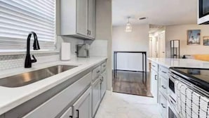 A modern kitchen with a large sink, white cabinets, and a view into the living area. - Charming Village Haven (Village)