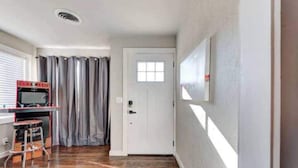 A room with a wooden floor, a white door, a window with curtains, and a small stool. - Charming Village Haven (Village)