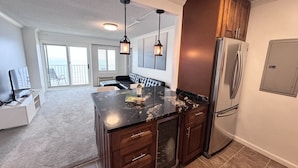 A modern kitchen with dark wood cabinets, a stainless steel refrigerator, and a marble countertop. - Panoramic Ocean Views | Modern Kitchen|Heated Pool 1304 (Virginia Beach)