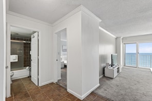 A hotel room with a bathroom, a balcony with a view of the sea, and a desk with a computer.