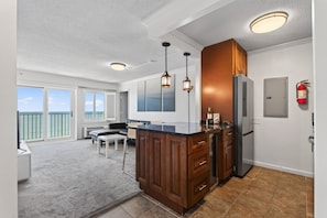 A modern kitchen with a central island, wooden cabinets, and a view to a balcony. - Panoramic Ocean Views | Modern Kitchen|Heated Pool 1304 (Virginia Beach)