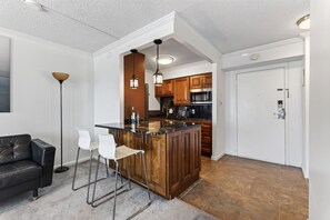 Une cuisine moderne dotée d’un îlot central, de meubles en bois et d’un four à micro-ondes encastré. On y trouve également un coin salon avec un canapé et des fauteuils.