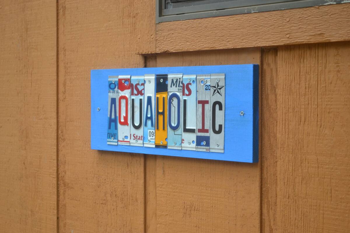 Ein blaues Schild mit dem Schriftzug 'AQUAHOLIC' an einer Holzwand.