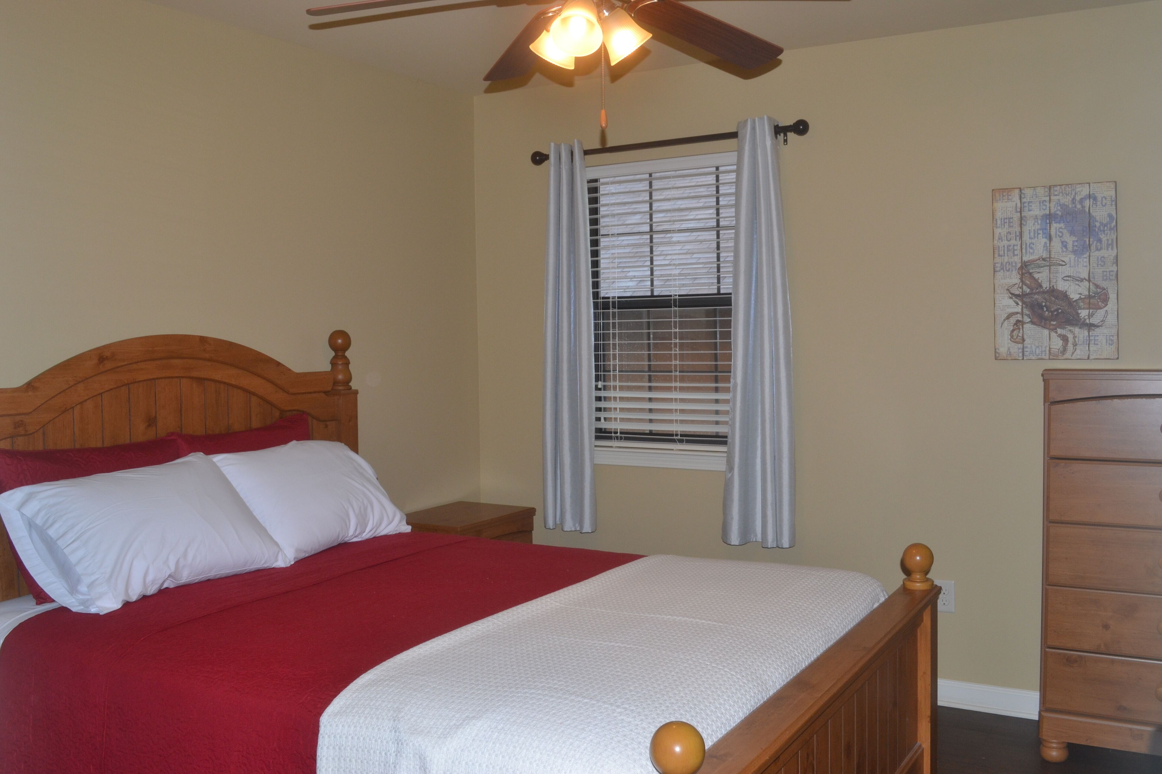 A bedroom with a wooden bed, a nightstand, a dresser, a ceiling fan, and a window with blinds.