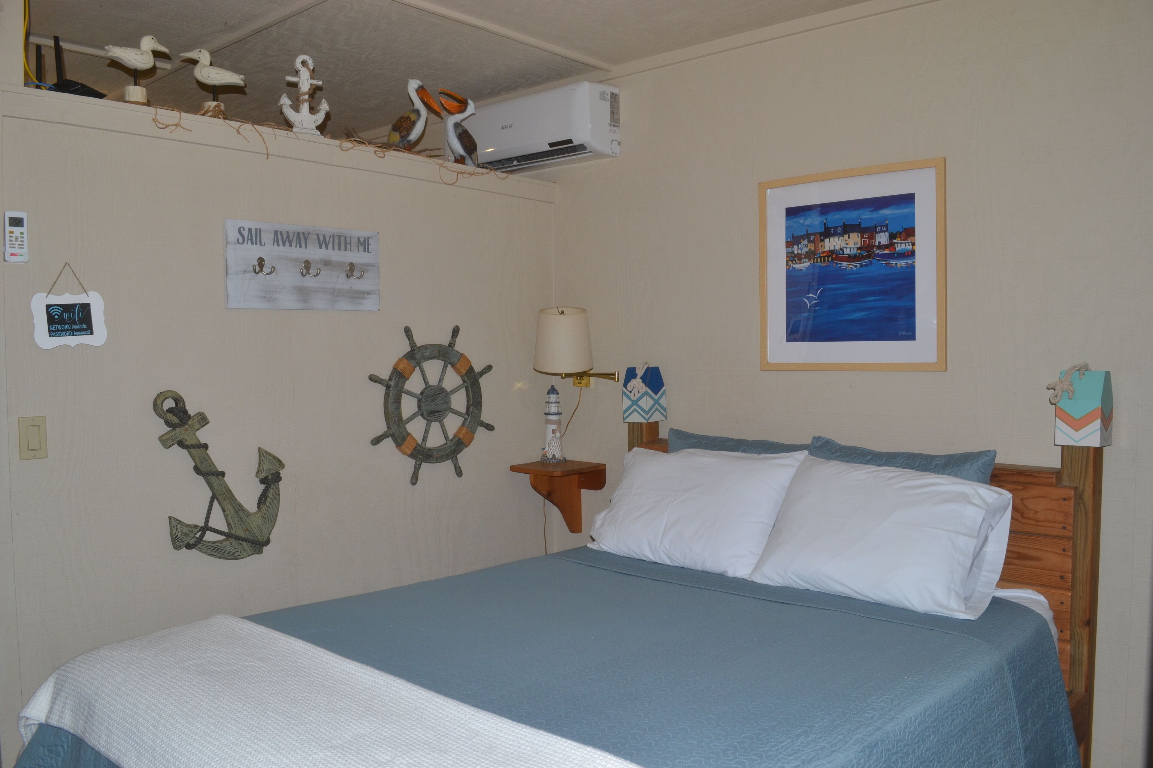 Een slaapkamer met een bed, een wandairconditioner, een lijst met foto en nautische decoraties.
