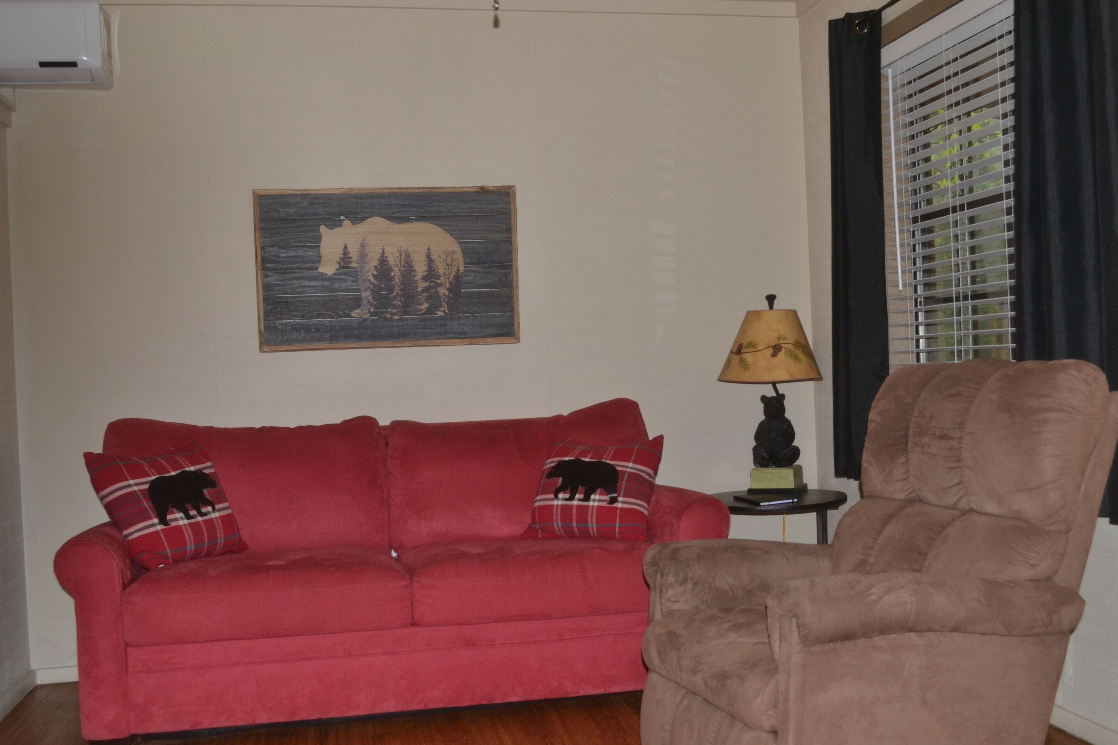 A living room with a red sofa, a brown armchair, a lamp, and a wall-mounted bear silhouette artwork.