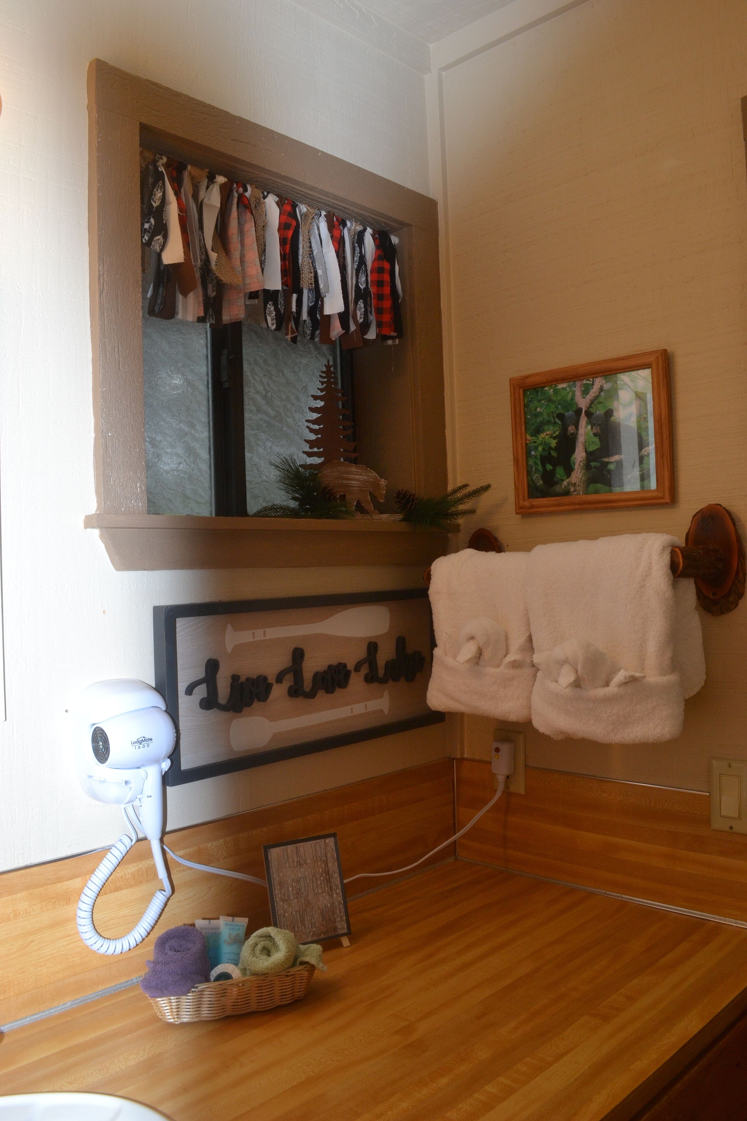 A bathroom with a wooden vanity, a towel rack with a white towel, a hairdryer, and a basket of toiletries.