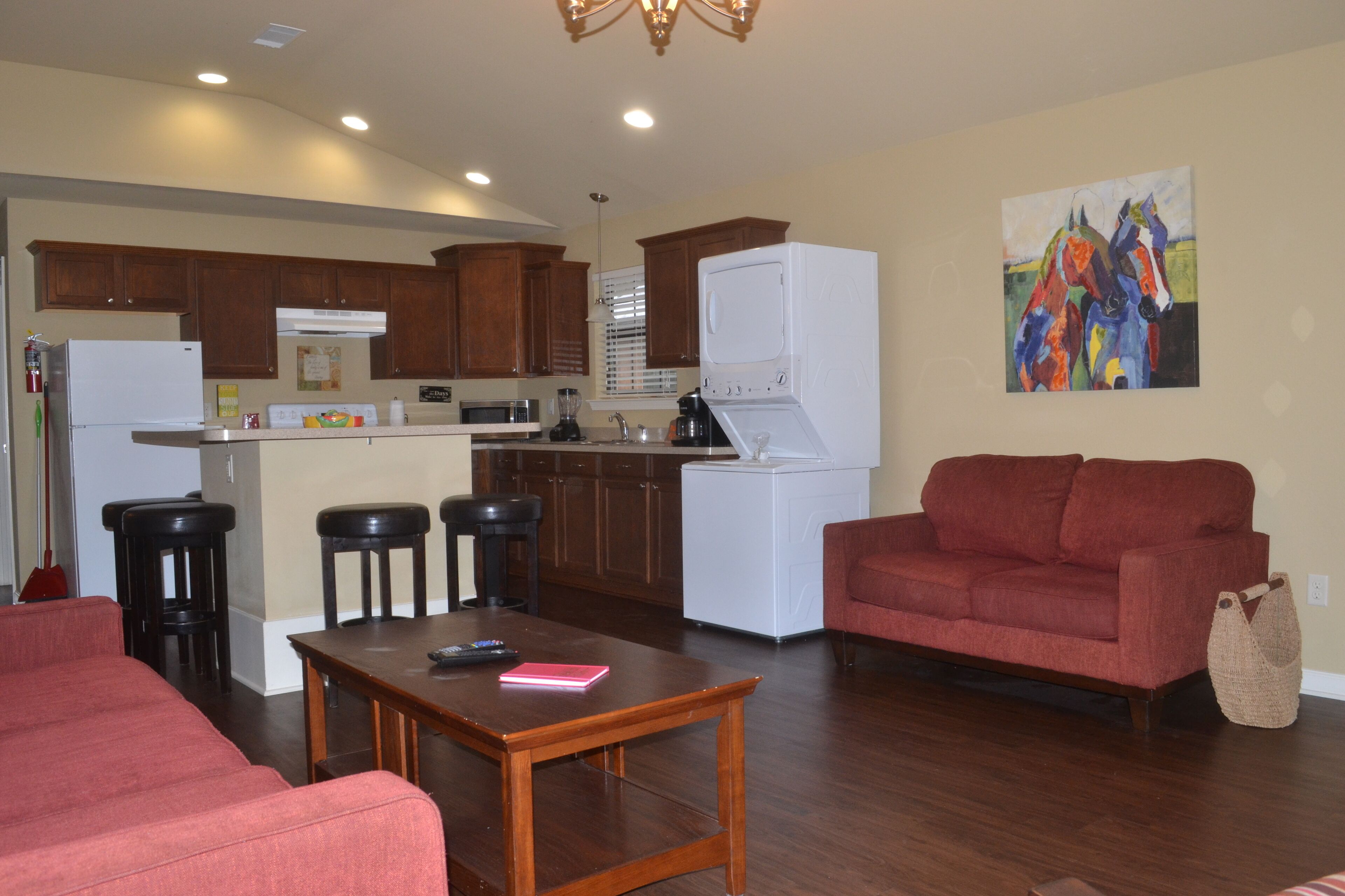 A modern kitchen with wooden cabinets, a white refrigerator, and a dining area with a red sofa and a wooden table.