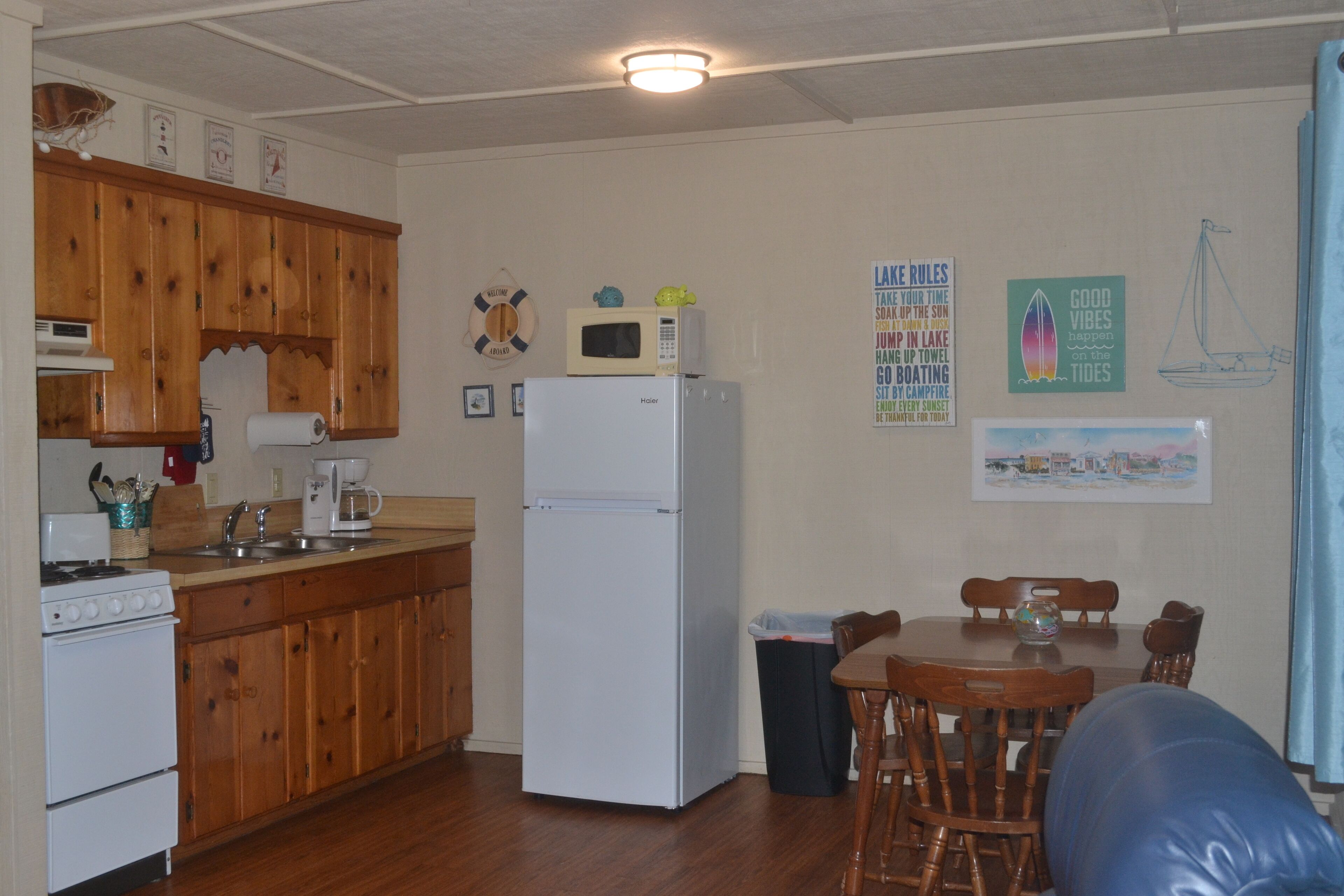 A kitchen with wooden cabinets, a white refrigerator, a stove, and a microwave. There is a dining table with chairs and a trash can.