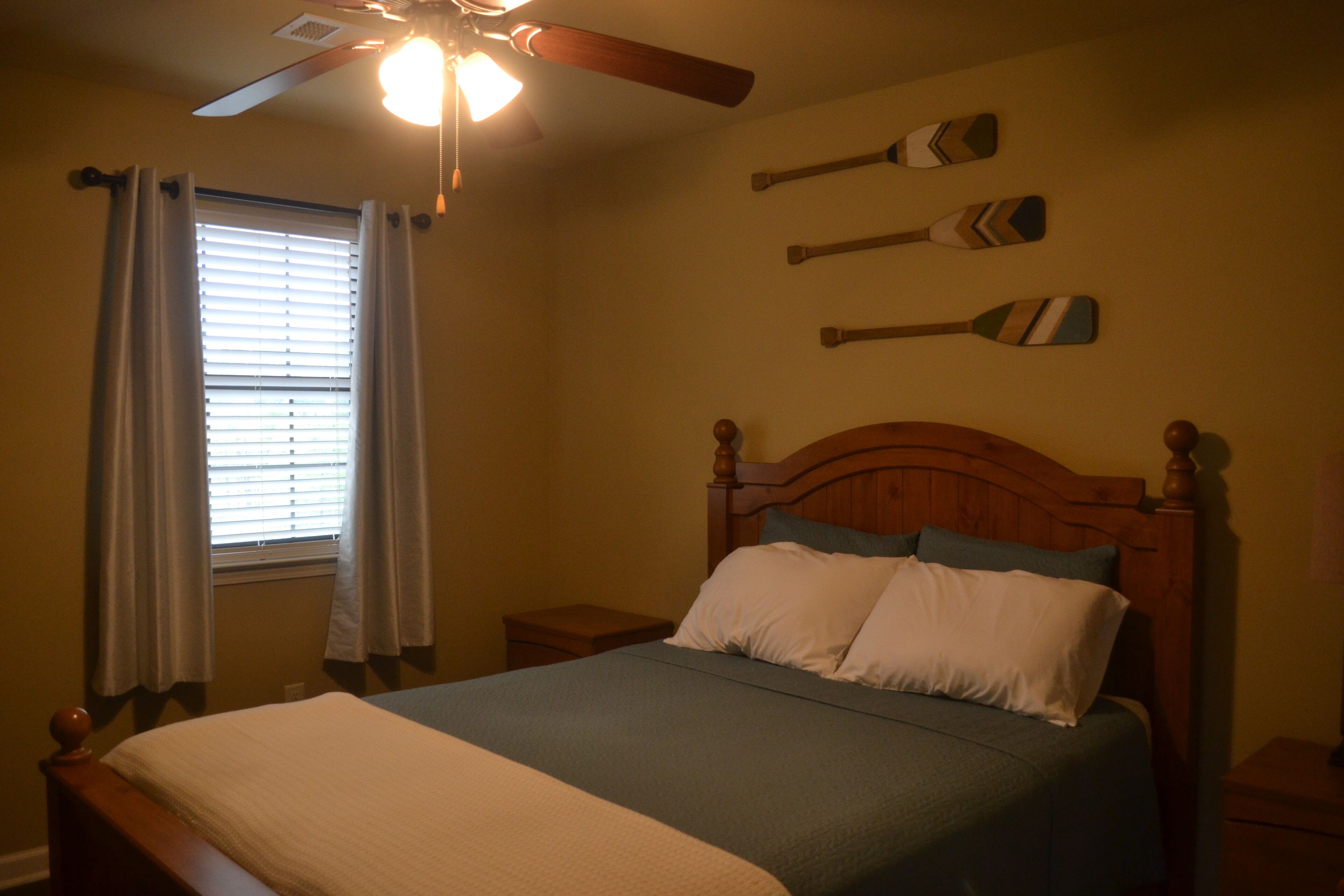 Un dormitorio con cama, ventilador de techo, ventana con cortinas y tres palas decorativas en la pared.