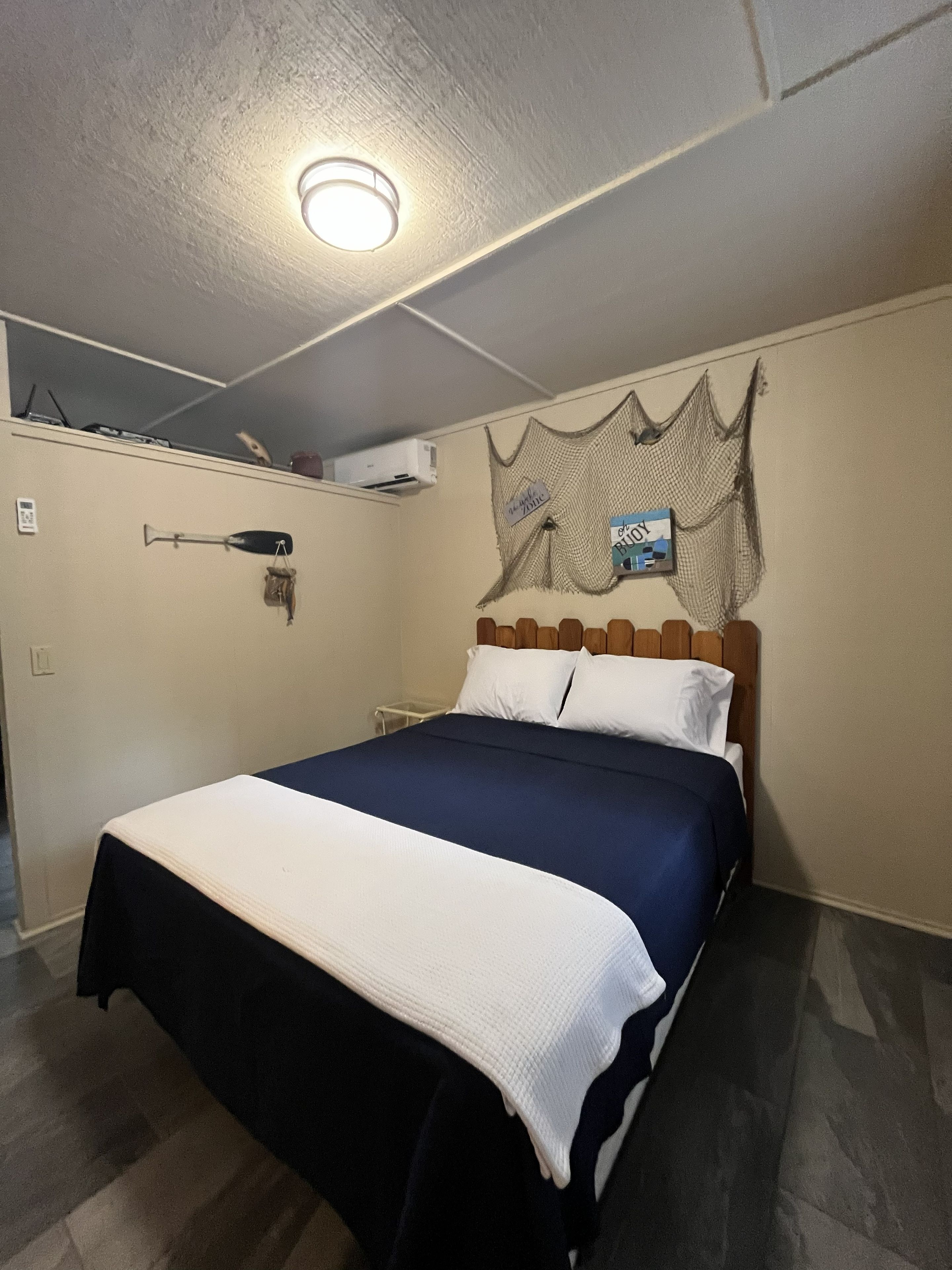 A single bed with a white and blue bedspread, a wooden headboard, and a ceiling light fixture.