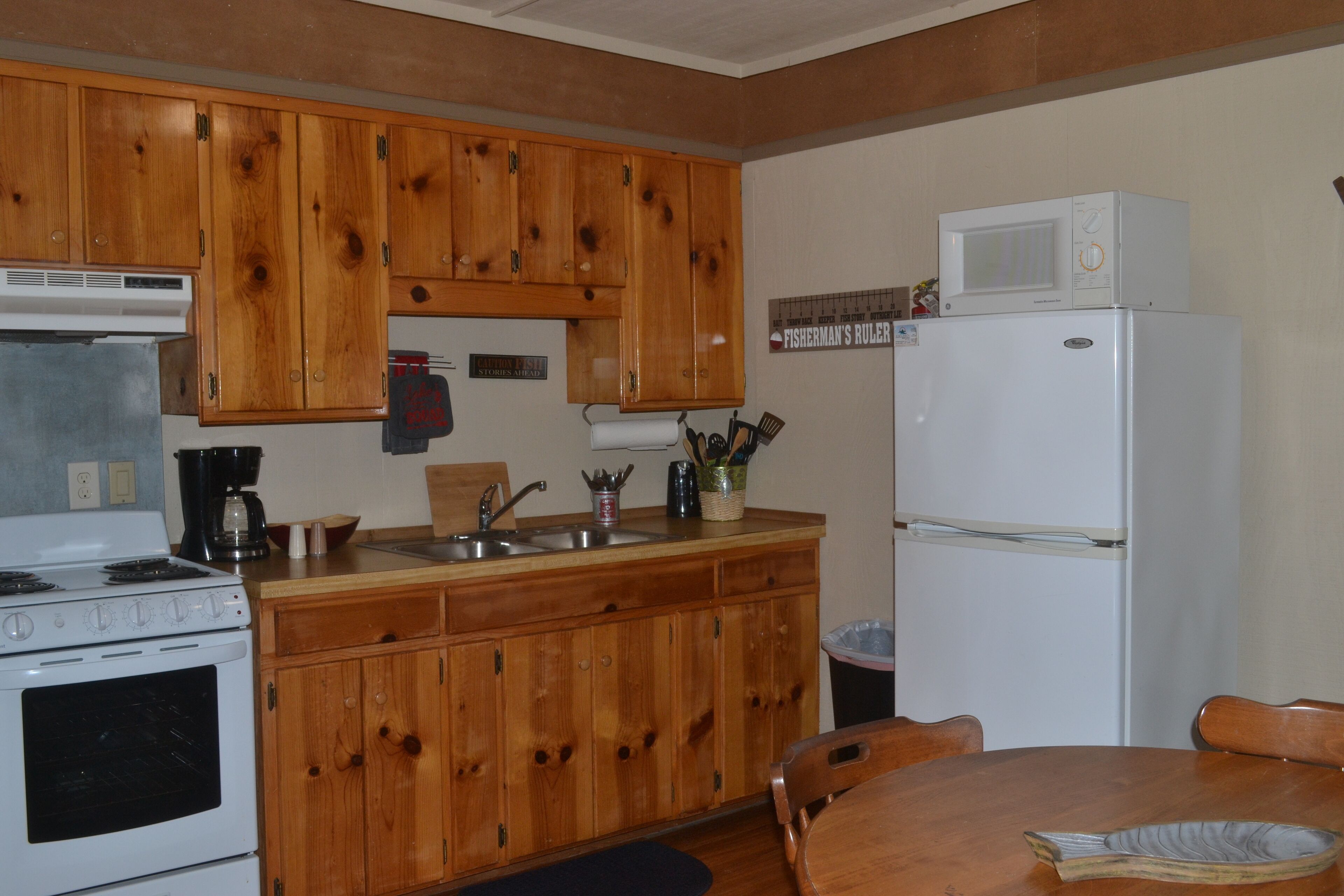 Una cocina con armarios de madera, una estufa blanca, un fregadero y un microondas sobre un refrigerador.