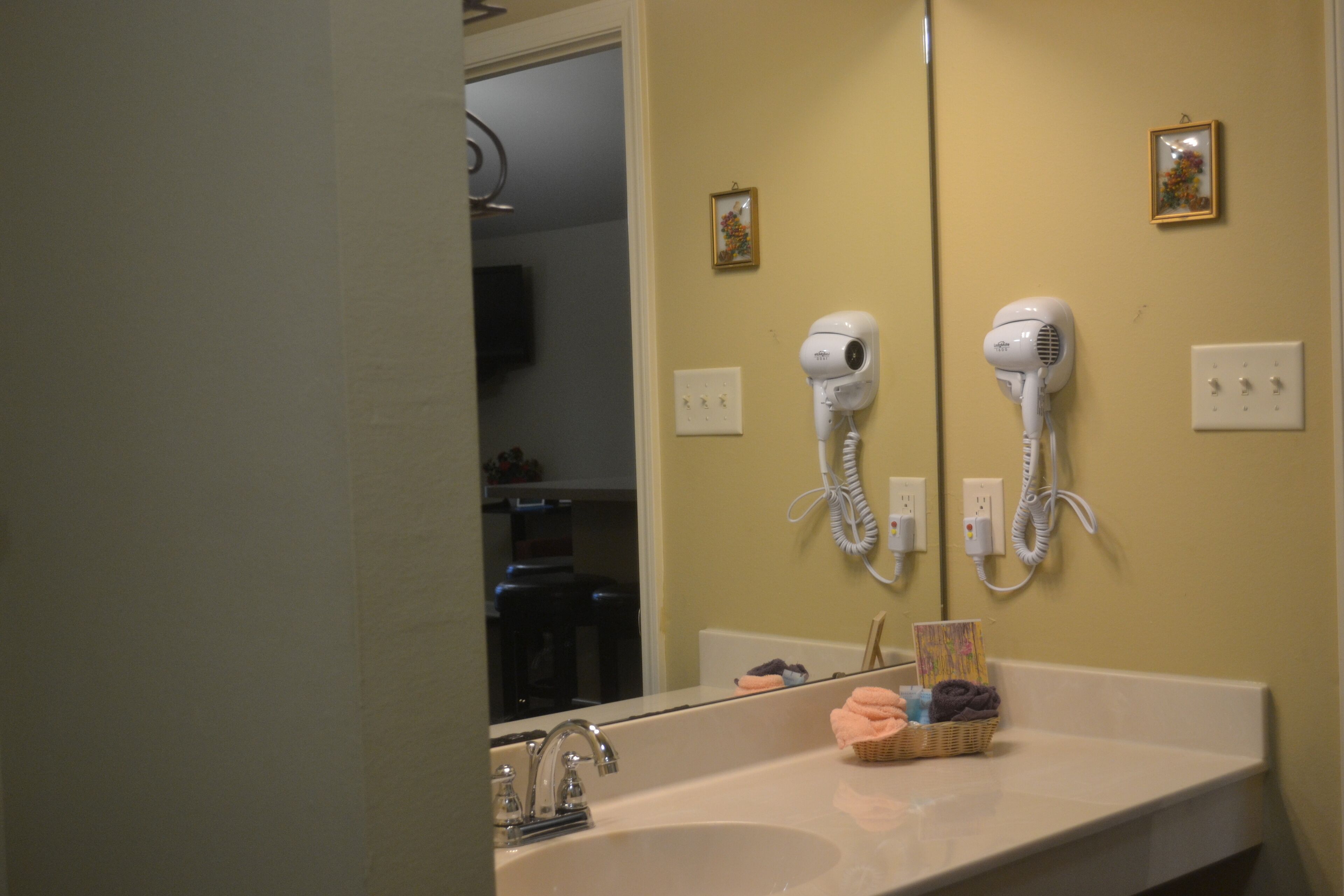 Un baño con un lavamanos, dos secadores de pelo sujetos a la pared y un espejo que refleja la habitación.