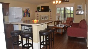 Una cocina con una isla central, taburetes de bar, una mesa de comedor y un sofá rojo.