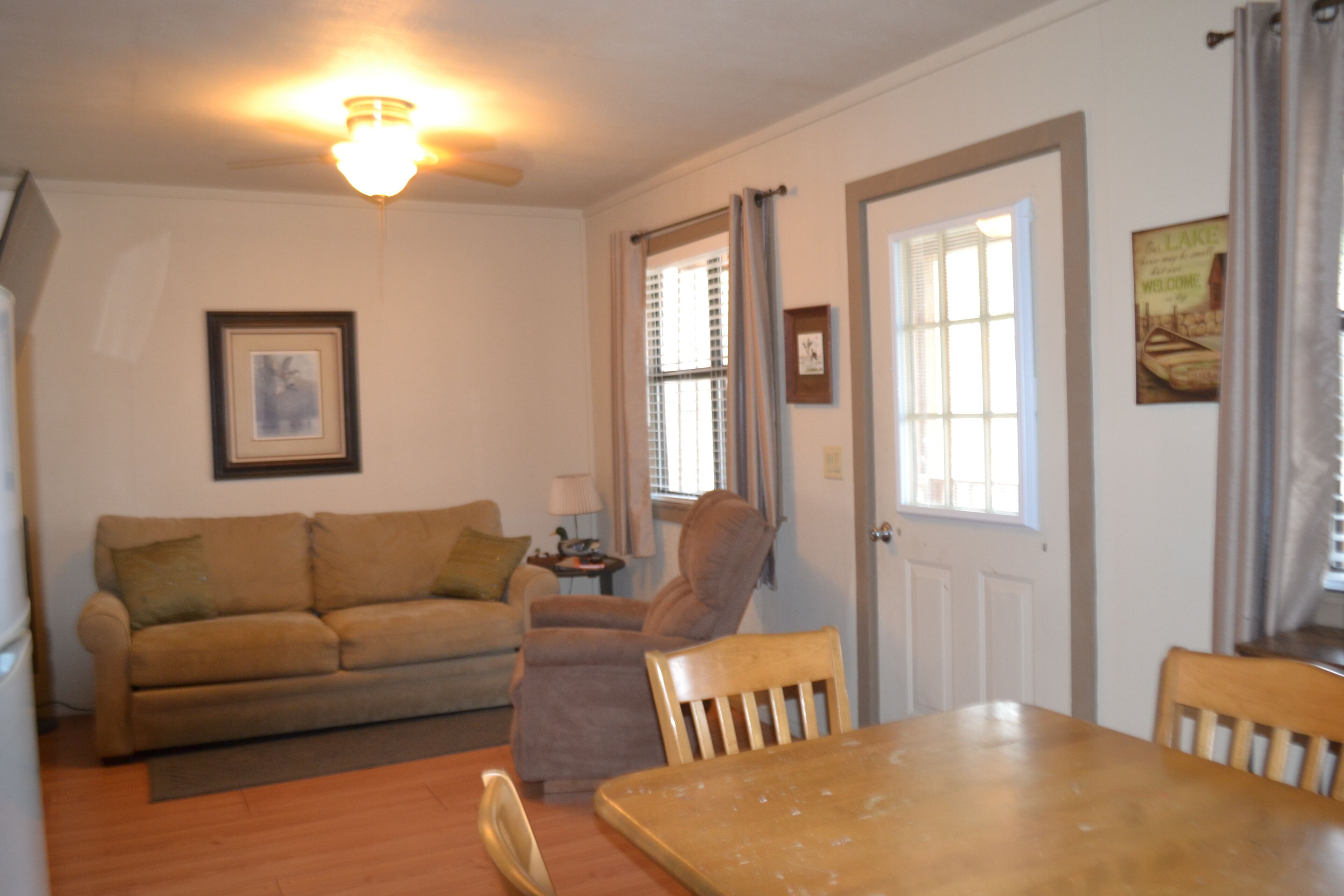 A living room with a sofa, a chair, a dining table, and a ceiling fan.