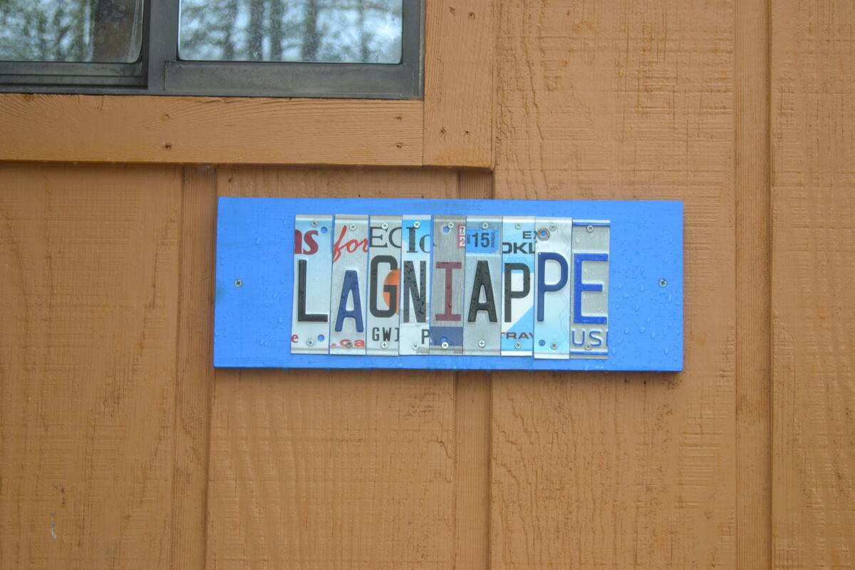 Ein blaues Nummernschild mit verschiedenen Aufklebern und Schriftzügen, an einer Holzwand befestigt.