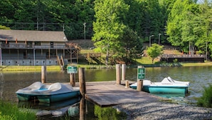 A dock with two boats, a building with a deck, and a sign indicating no swimming in the lake. - Hawk Ridge Haven | Sleeps 4 | Hiking | Fishing | Community Pool (Deep Gap)
