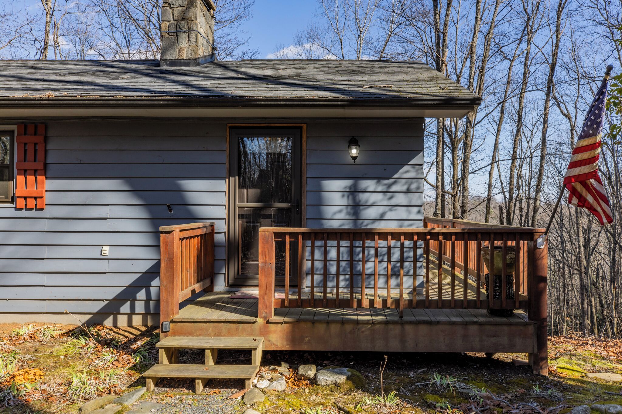 A wooden cabin with a porch, a chimney, and an American flag.