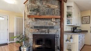 A stone fireplace with a metal vent, a potted plant, and a kitchen area with cabinets and a countertop. - Hawk Ridge Haven | Sleeps 4 | Hiking | Fishing | Community Pool (Deep Gap)