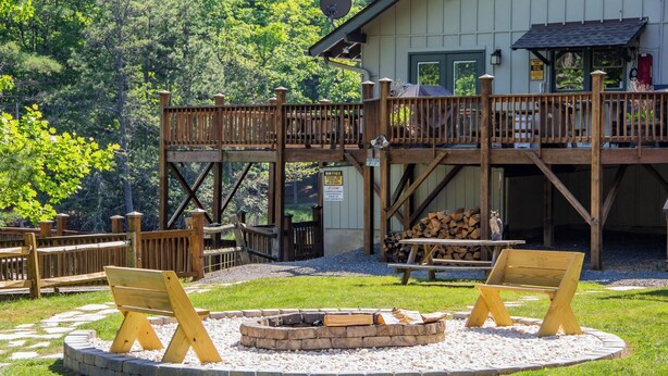 A wooden deck with a fire pit and seating area, surrounded by a stone border. - Hawk Ridge Haven | Sleeps 4 | Hiking | Fishing | Community Pool (Deep Gap)