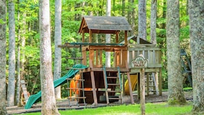 A wooden play structure with a slide and climbing area, surrounded by trees. - Hawk Ridge Haven | Sleeps 4 | Hiking | Fishing | Community Pool (Deep Gap)