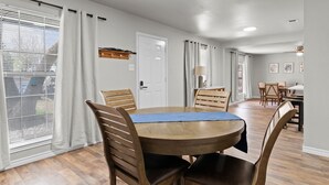 Ein Essbereich mit einem runden Holztisch, vier Holzstühlen, einer blauen Tischdecke und einer weißen Tür.
