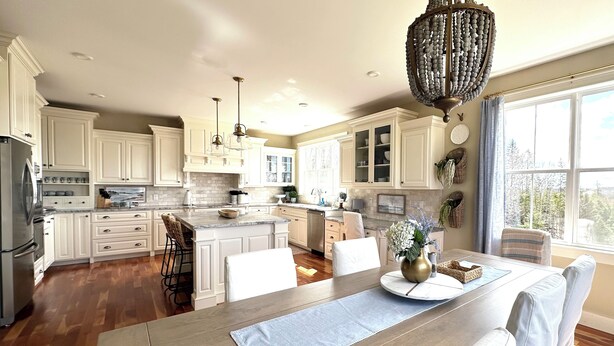 A spacious kitchen with white cabinetry, a large island, and a dining area with a wooden table and white chairs. - Luxury Rental Located In New Glasgow, Minutes To Amazing Restaurants and Beaches (New Glasgow)