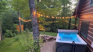 Un bain à remous dans un jardin, avec une terrasse en bois, entouré de verdure et illuminé de guirlandes lumineuses.