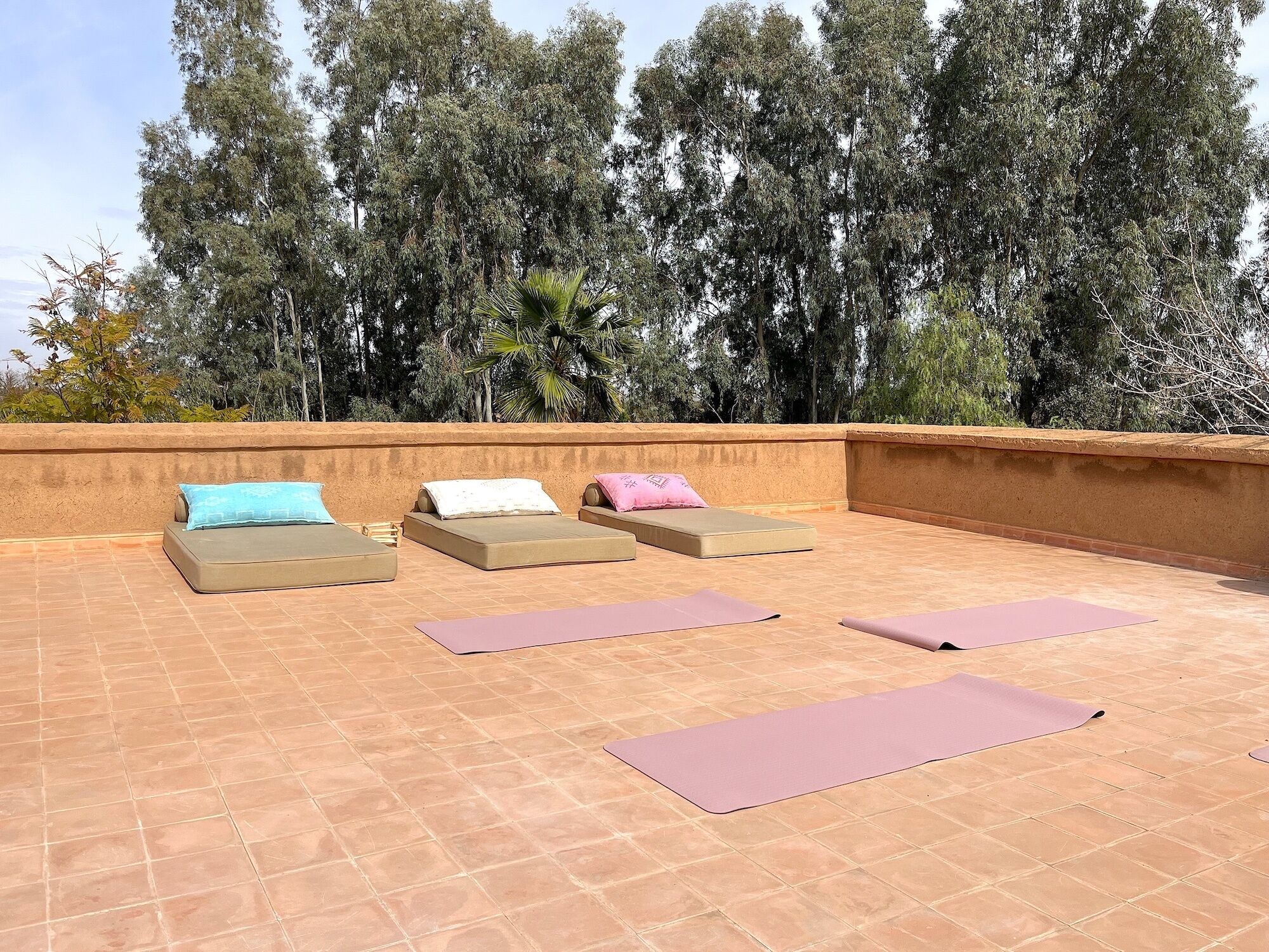 Una terraza en la azotea con cuatro sillones de descanso, cada uno con una almohada, y dos esterillas de yoga en el suelo.