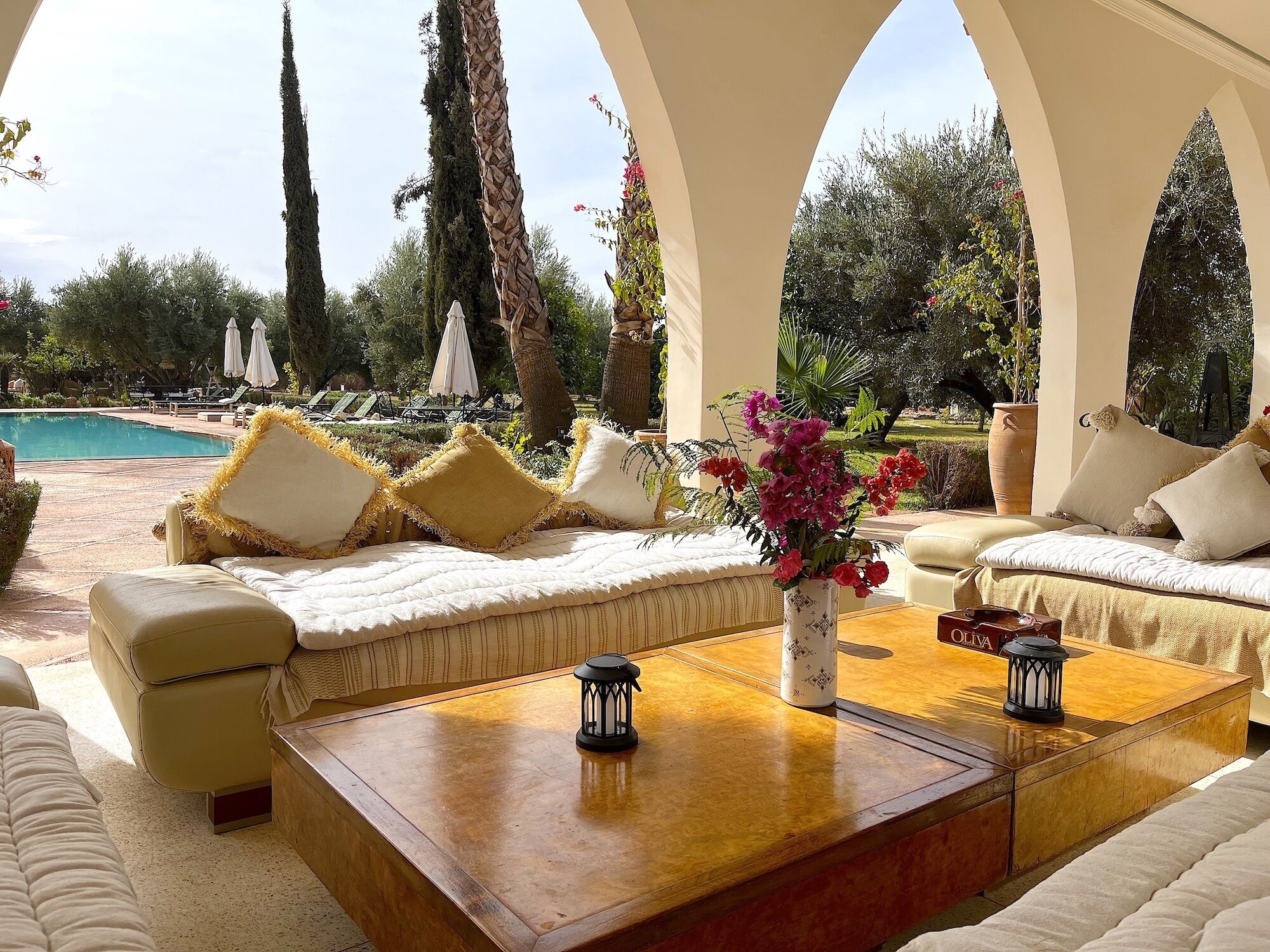 A luxurious outdoor seating area with a pool view, featuring sofas, a coffee table, and a vase with flowers.
