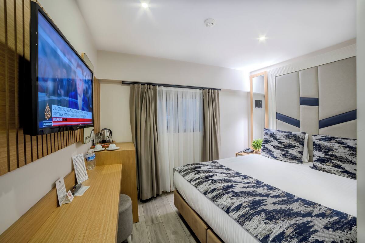 A hotel room with a bed, a desk, a television, and a window with curtains.
