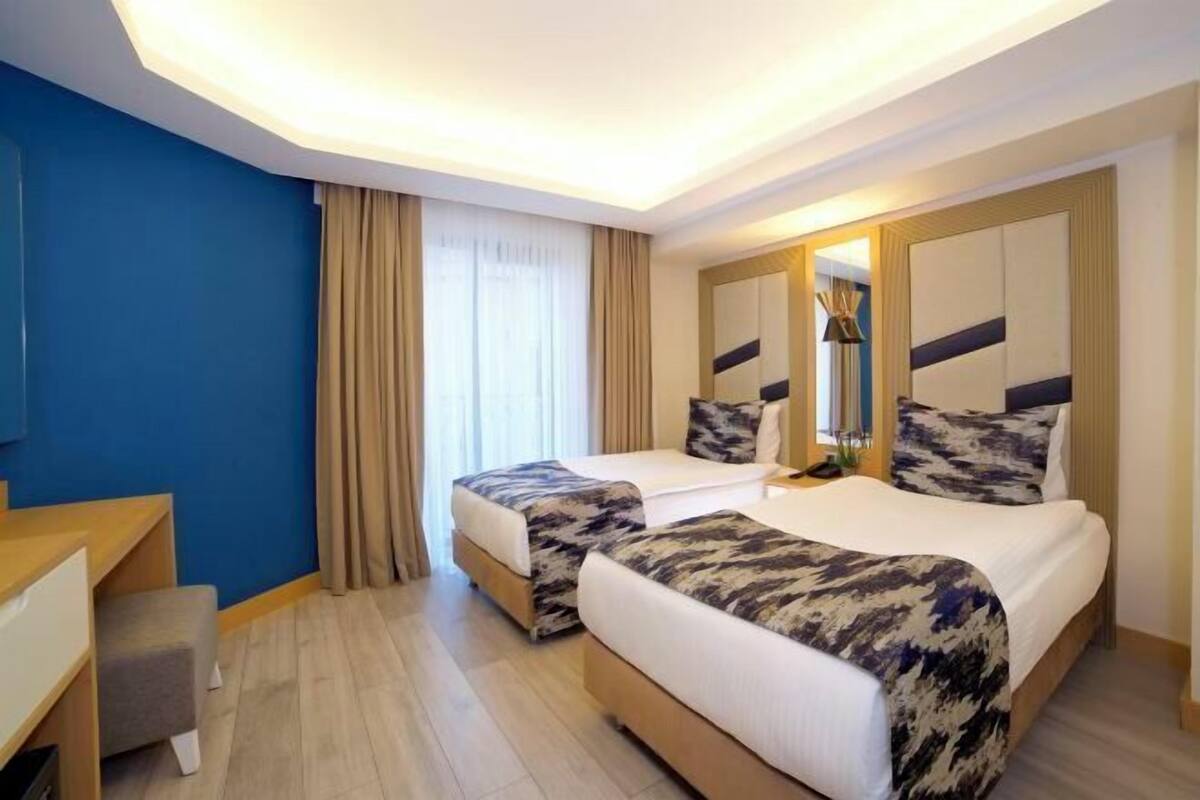 A hotel room with two beds, a desk, a chair, a mirror, and a window with curtains.