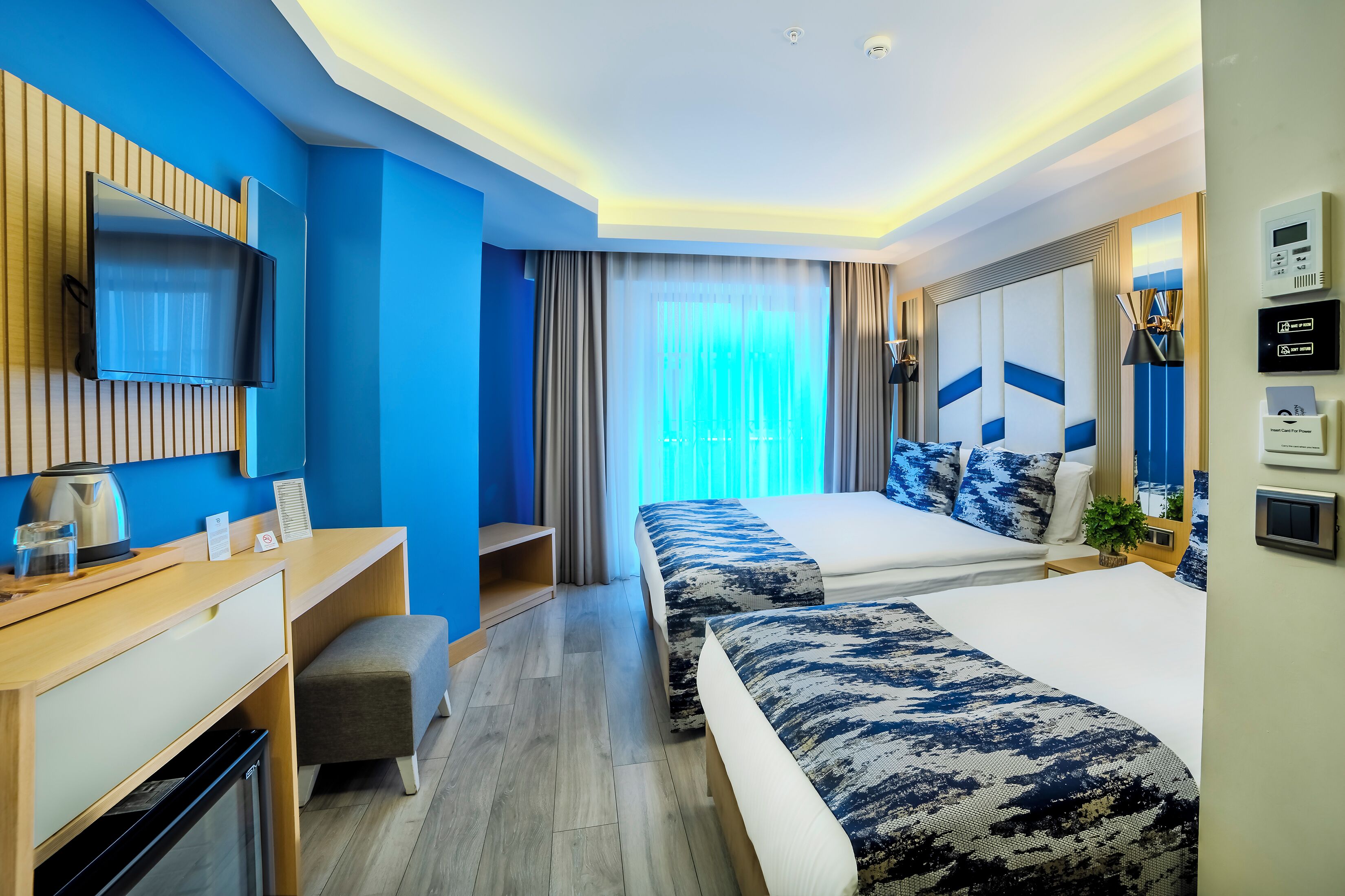 A modern hotel room with a flat-screen TV, a desk, a sofa, and a bed with patterned bedding.