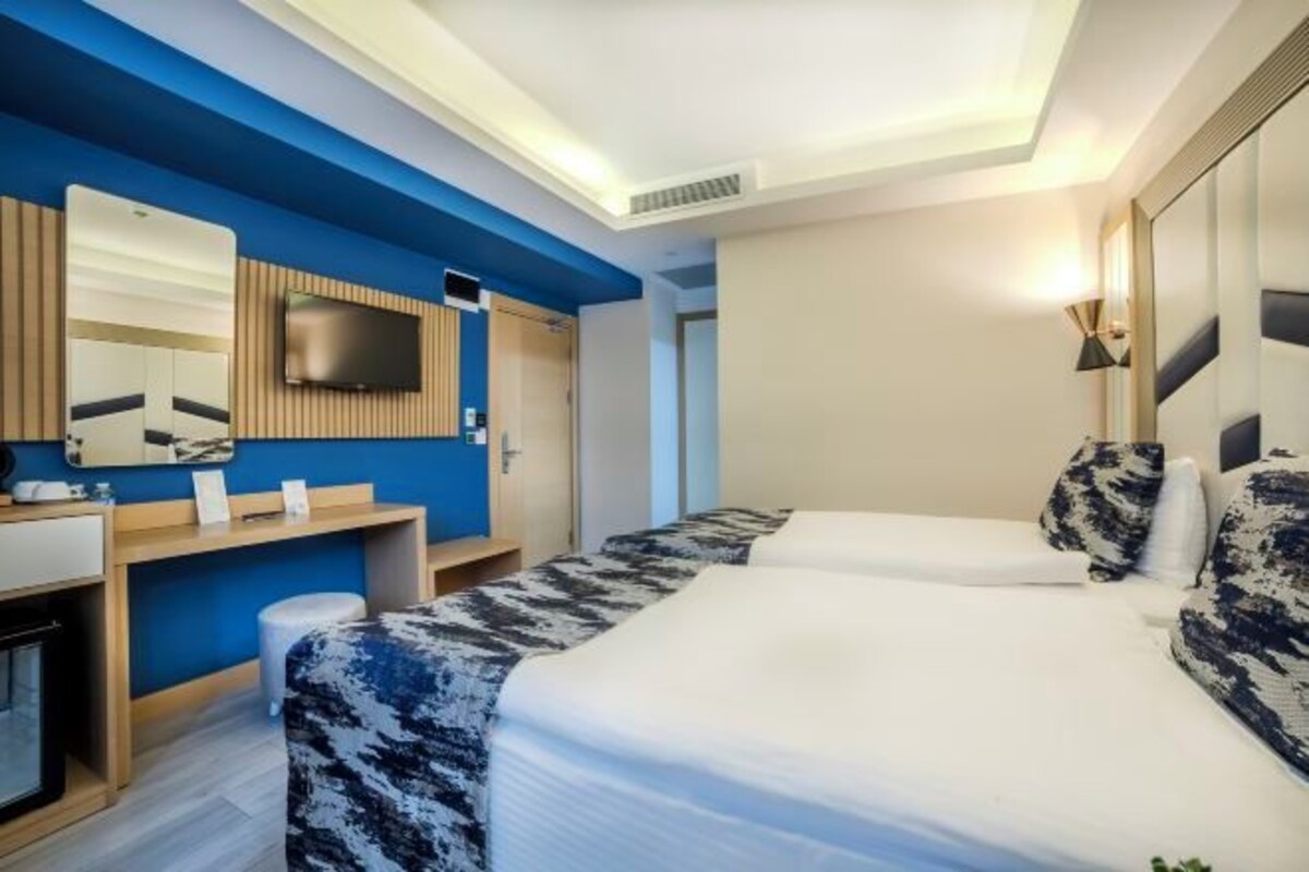 A hotel room with a bed, a desk, a mirror, and a TV.