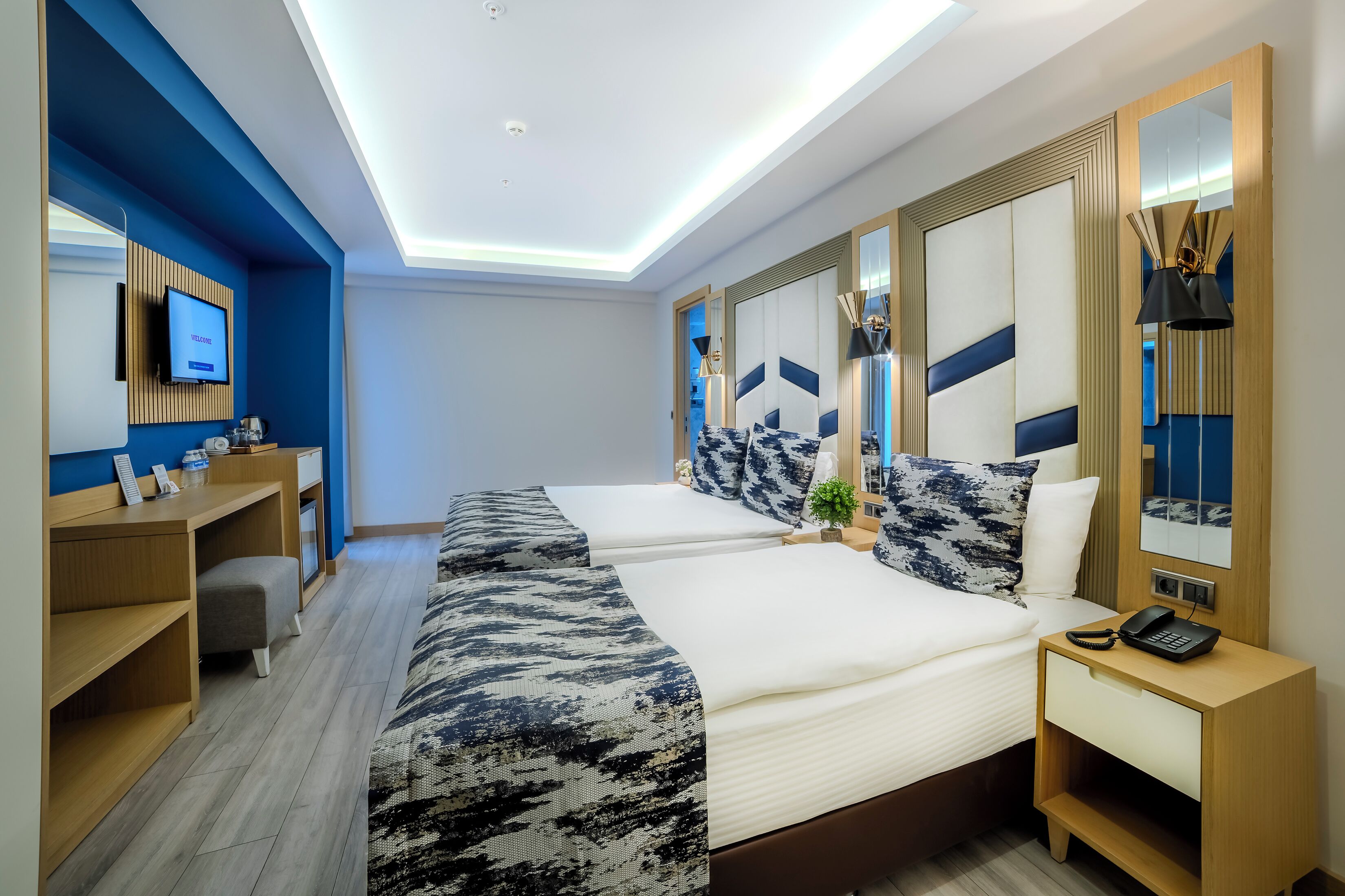 Una habitación de hotel con cama, mesita de noche, lámpara y televisor en la pared.