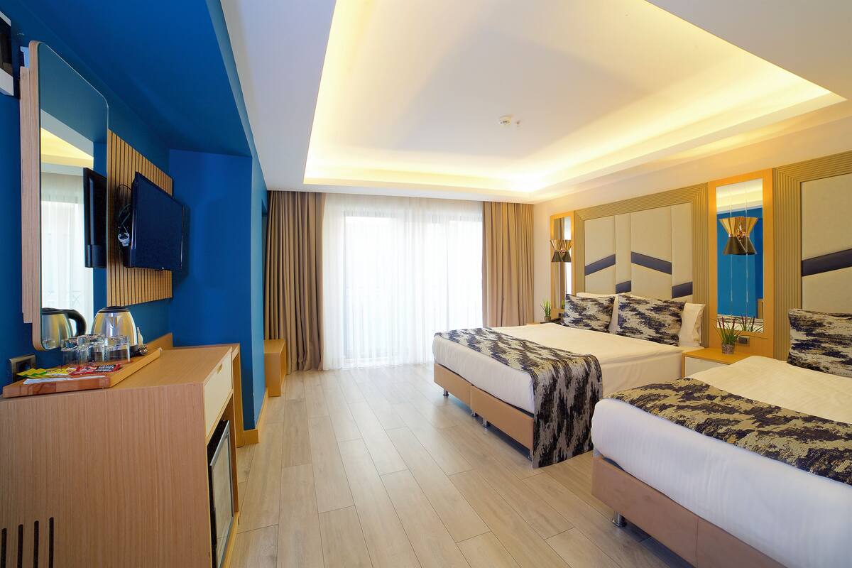 A hotel room with a bed, a desk with a TV, and a window with curtains.
