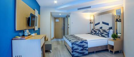 A modern hotel room with a bed, bedside table, TV, and a desk with a chair.