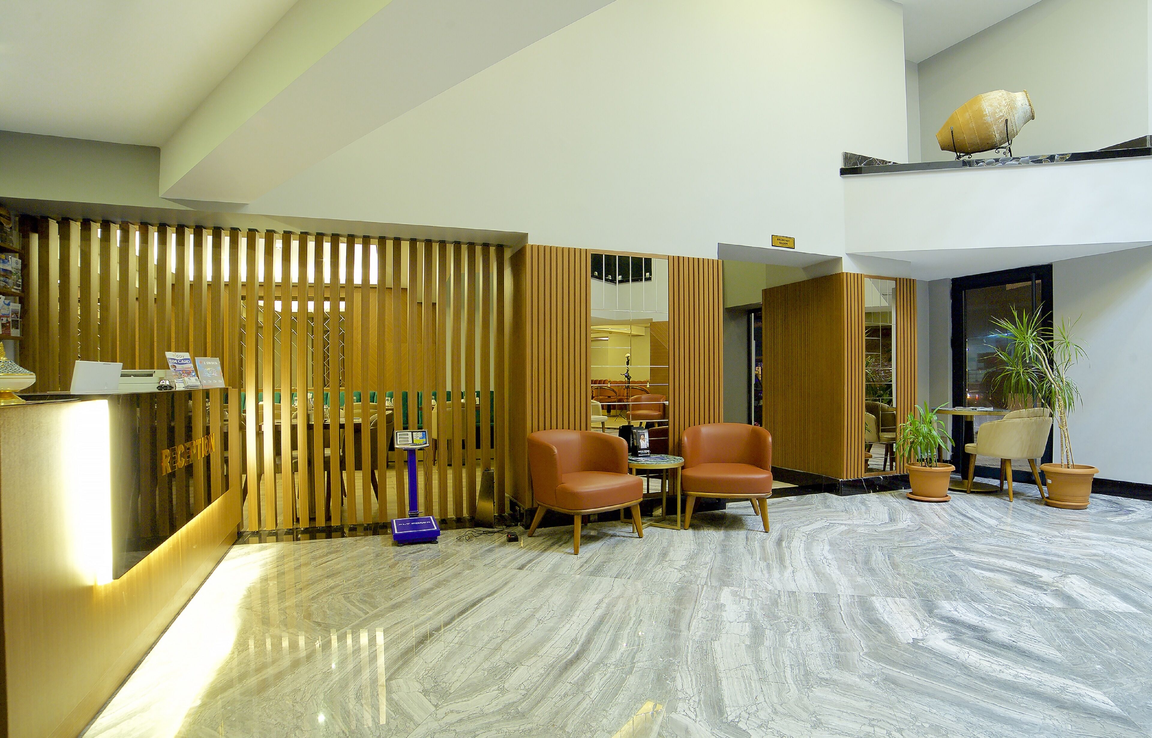 A reception area with a wooden partition, two leather chairs, a reception desk, and potted plants.