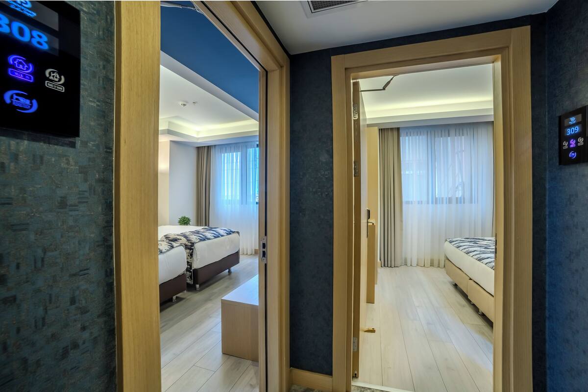 A modern hotel room with a digital lock, a bed, a bedside table, and a large window with curtains.