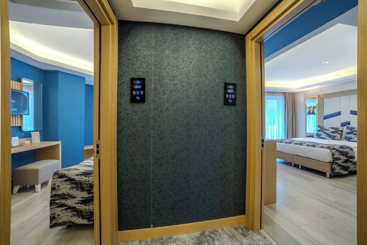 A modern hotel room with a large bed, a desk with a chair, a small seating area, and a large mirror.