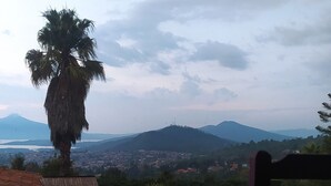 Vista desde un balcón con una palmera, una silla y una cadena montañosa distante.