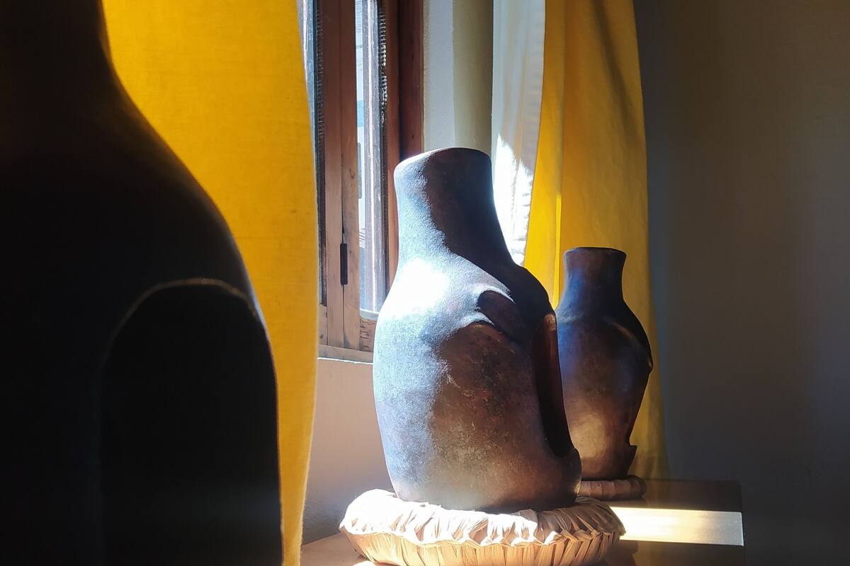 A room with a window, a table with pottery, and a yellow curtain.