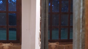 Un rincón de una habitación con suelo de baldosas, un banco de madera y una ventana que da a árboles.