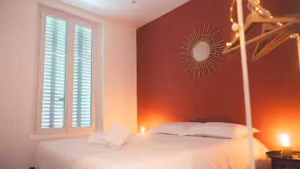 Un dormitorio con cama, lámpara de pared y ventana con persianas.