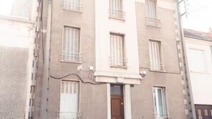 Un edificio de varios pisos con fachada color beige, múltiples ventanas con contraventanas y una puerta de entrada visible.