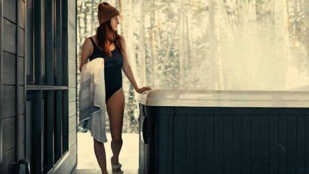 A woman walking towards a hot tub in a cabin with a view of a forest. - Au Chalet Calme (Lac-Superieur)