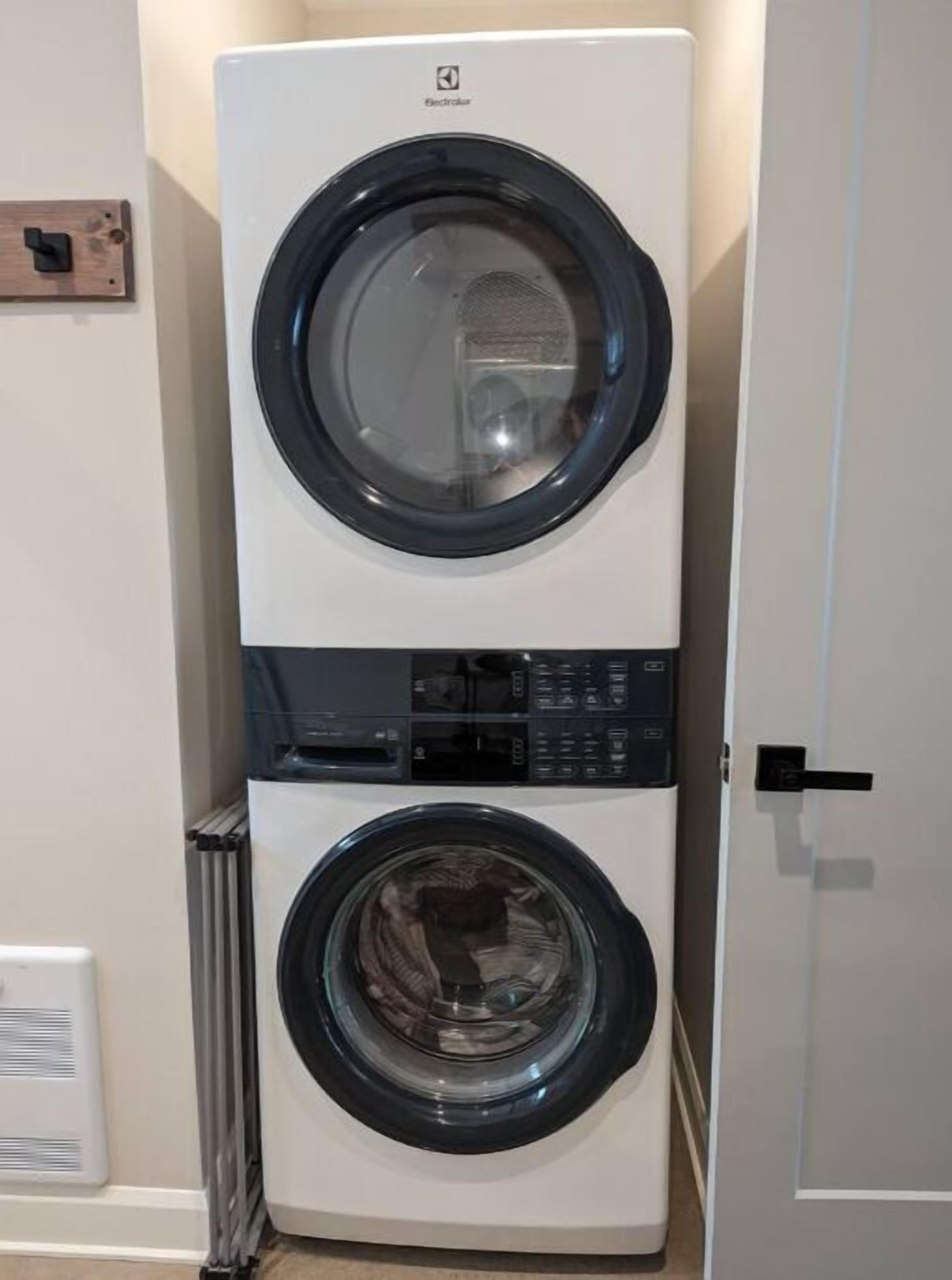 A stacked washer and dryer unit in a room with a white door and a radiator.