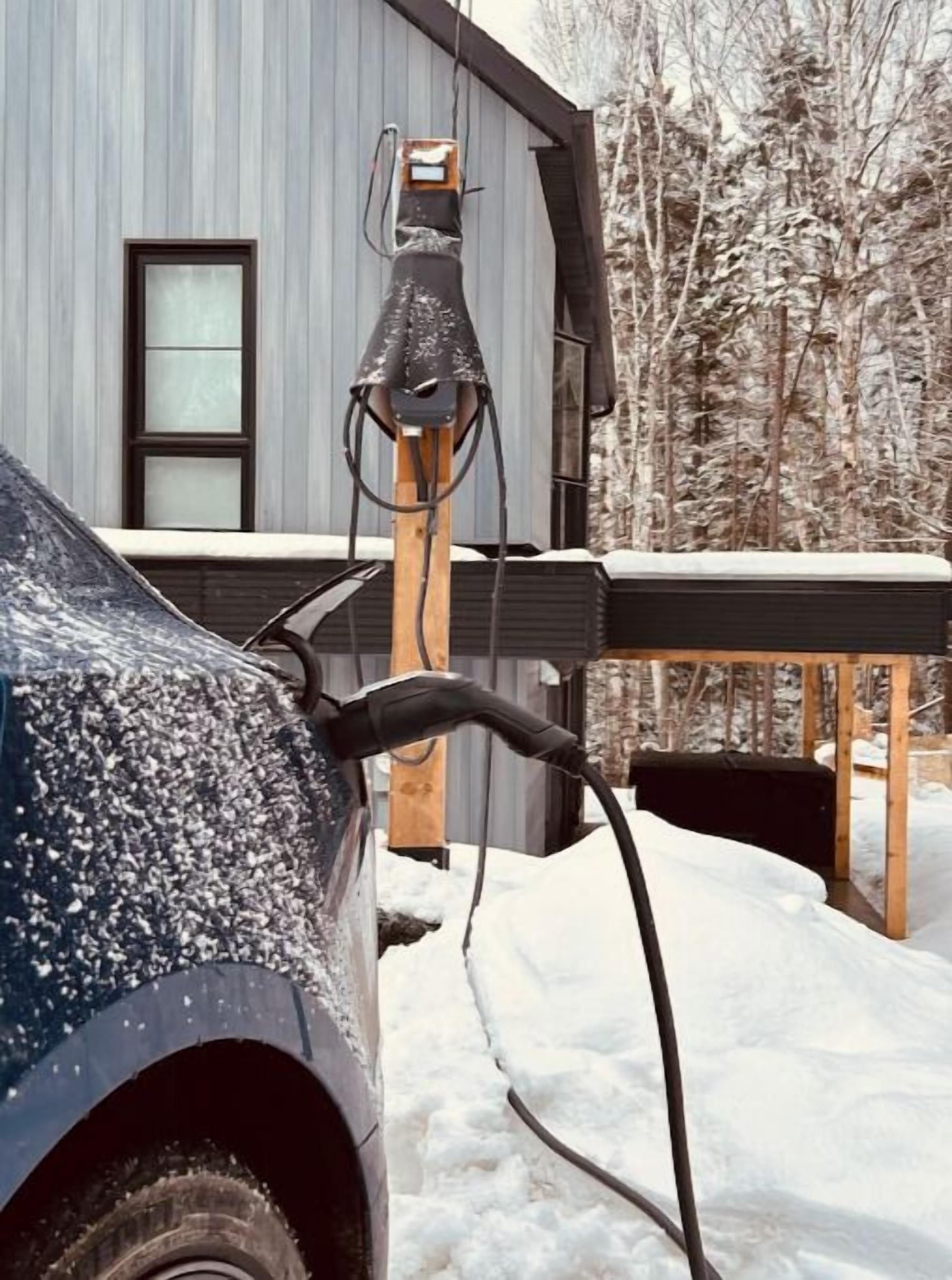A car parked in a snowy area with a charging station attached to a building.